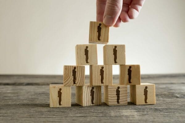 Hand building pyramid from blocks with businessman figures on them