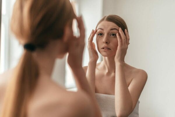 Woman in a towel looking at her reflection in a mirror as she reflects on procrastination