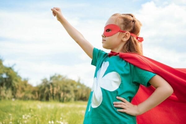 adorable child in superhero costume with outstretched arm in summer field is a superwoman