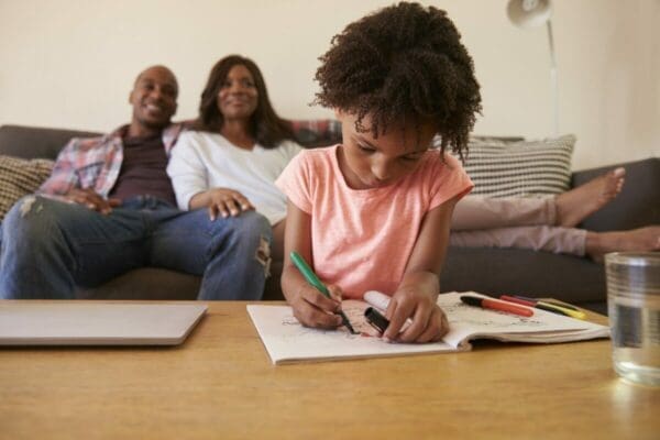 African American parents Watch TV As Daughter Colors In Picture Book