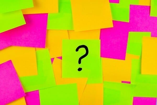 Question mark drawn on a post it note with neon yellow pink and green post it notes background