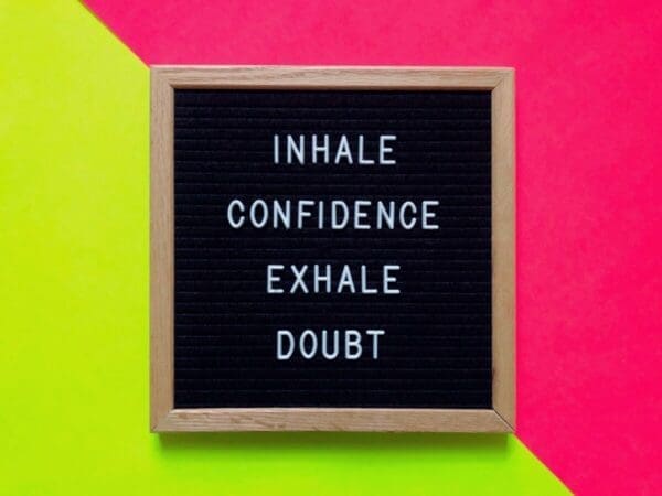 Inhale confidence exhale doubt quote on blackboard with a pink and yellow background