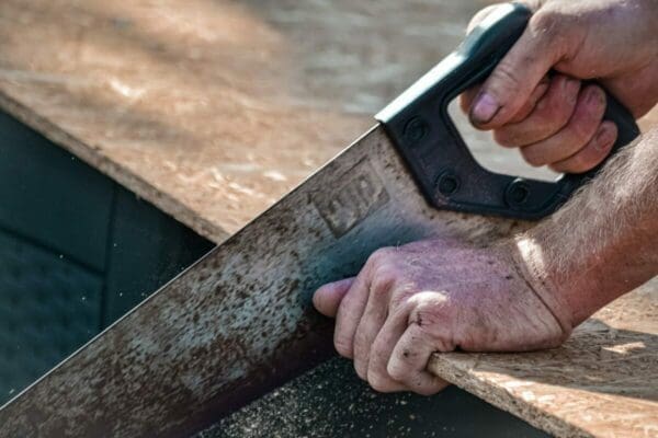 Close up of man's hands using a saw on a wooden plank 