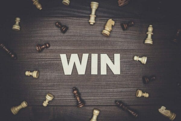 Word win on wooden background with chess pieces surrounding