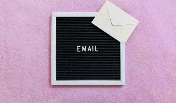 The word email written on a felt board on a pink background with an envolope
