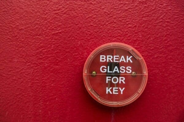 Emergency break glass container with key inside against a red wall