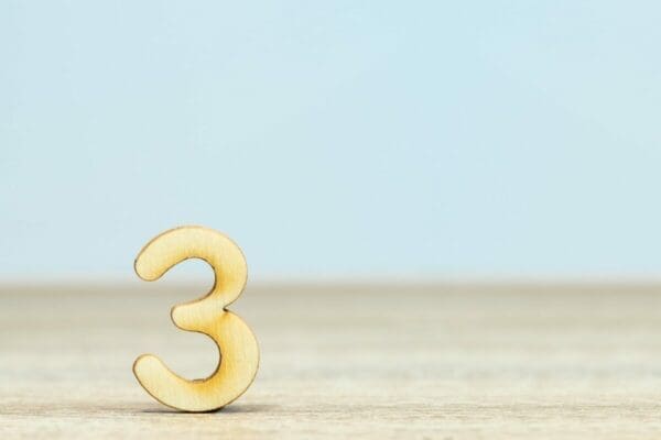 Gold number three on a wooden surface against blue background 