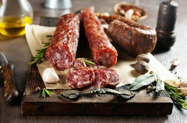 Some salami on a wooden board with garnishes