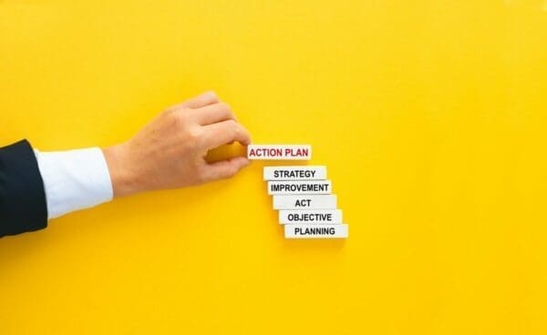 Building blocks of words with action plan then strategy, improvement, act, objectives, and planning on yellow background