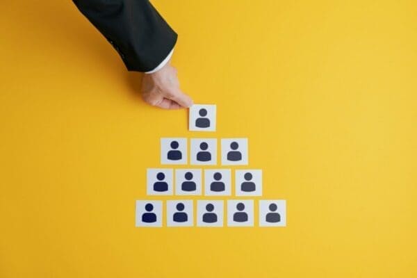 Hand of businessman forming business hierarchy made of employee icon images on a yellow background