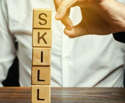 SKILLS spelled with wooden blocks staked in a tower with businessman in the background