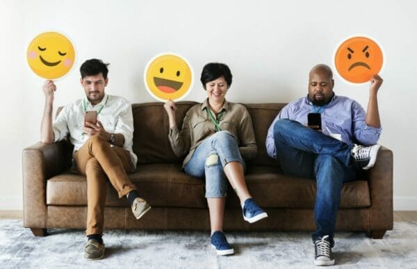 Diverse people sitting and holding emojis logos are instant messaging on ther phones