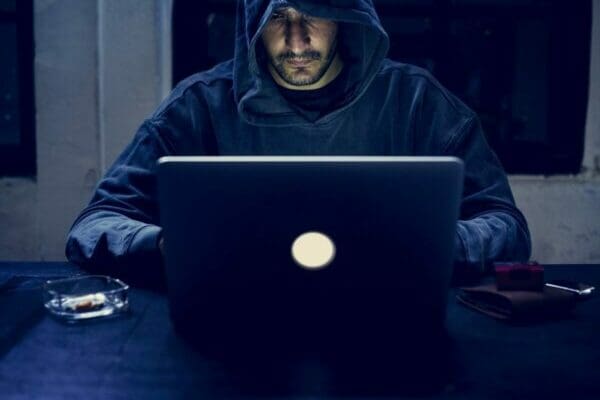 Hacker wearing a hood in the dark while working on a laptop doing cyber crime