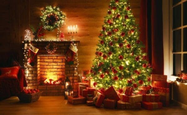 Christmas Tree with many gifts next to lit fire place in a warm cozy room