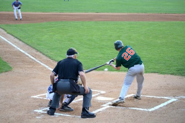 Minor league baseball team playing baseball game with umpire. Batter hits the ball with baseball bat