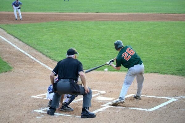 Minor league baseball team playing baseball game with umpire. Batter hits the ball with baseball bat