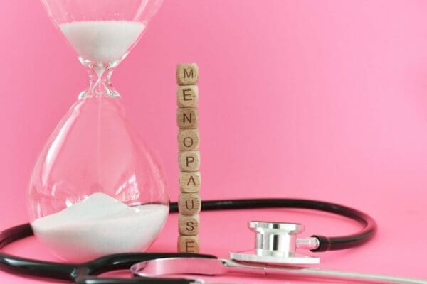 Menopause with stethoscope and hourglass on pink background represents going through the change