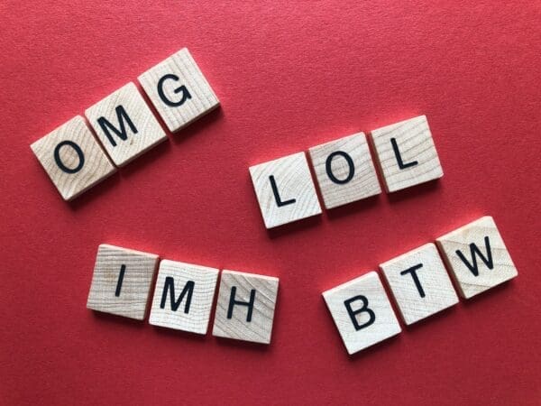 Wooden tiles with sang word abbreviations OMG, LOL, IMH, and BTW on red background