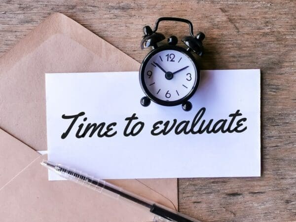 Text time to evaluate written on white paper with a pen, brown envelope and alarm clock