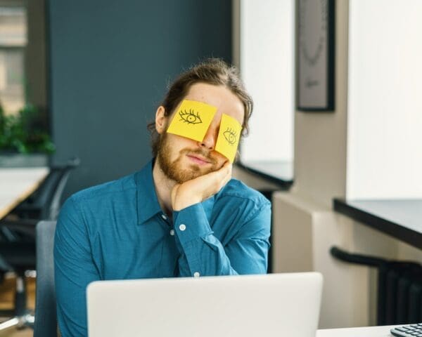 Problem employee with eye drawings on a yellow sticky note over his eyes is funny