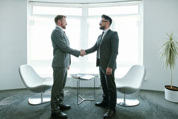Two young successful businessmen in suits shaking hands after negotiation