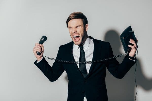 Angry businessman in suit screaming with phone in hands on white background