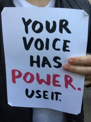 Man holding hand-written sign saying your voice has power use it