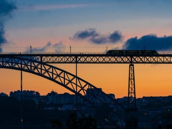 Black metal bridge with a moving train against backdrop of sunset