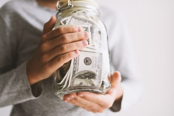 Child holding glass jar stuffed with money notes