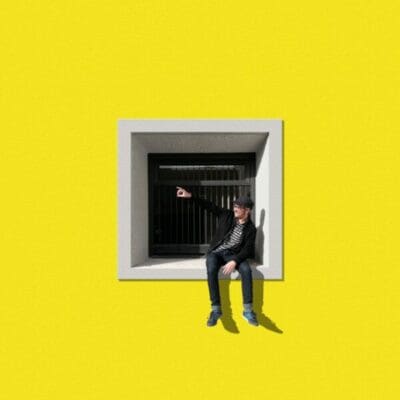 A man sat in a window against a yellow background