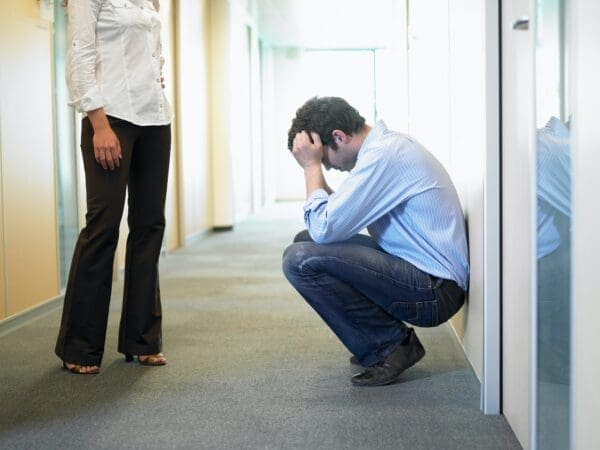 Businessman crouching in a corridor with head in hands is dealing with a personal problem at work