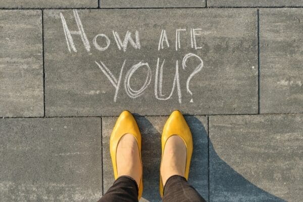 How are you written on gray sidewalk above woman's yellow shoes