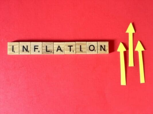 Inflation spelled with wooden word scramble cubes next to yellow up arrows