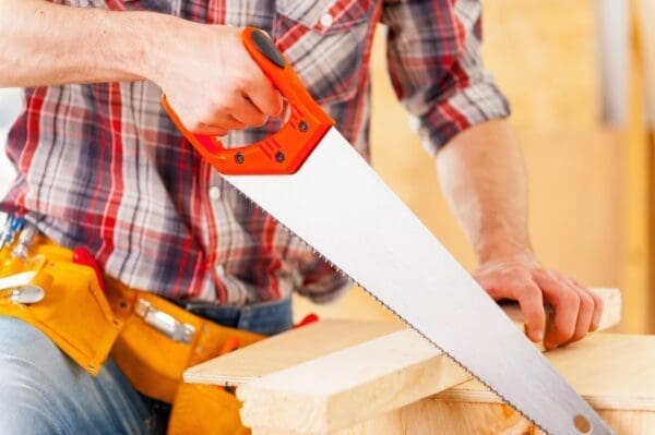 Close-up of handyman using saw in workshop to cut wood