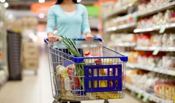 Woman pushing shopping trolley with food through a supermarket aisle