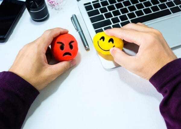 Two hands each holding an angry face and a smiley face emoticon on an office desk