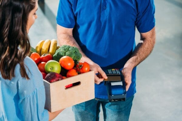 Delivery man using card and payment terminal while woman holding groceries in box
