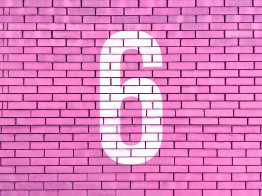 White number 6 on a pink brick wall