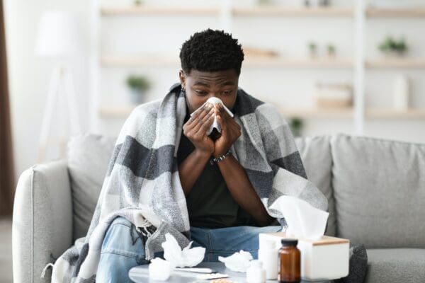 Man sitting on sofa sneezing with tissues in a blanket