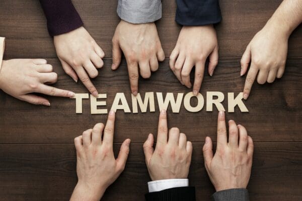 Hands of team members touching each letter of teamwork cutout on a wooden table