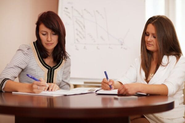 Two businesswomen taking notes on a wooden table