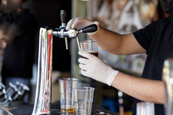 Barman pouring fresh beer in plastic cup behind the bar