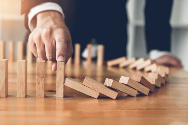 Businessman finger stopping a falling dominoes effect