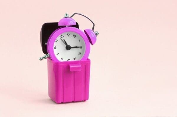 Pink alarm clock in a pink bin represents wasted time