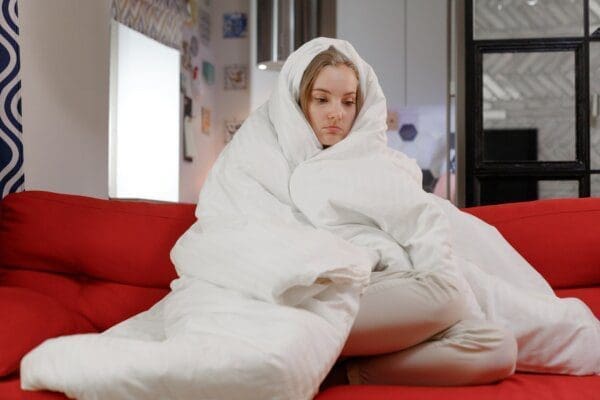 Woman warming up under the covers in bad cold weather, having a cold and lonely mood