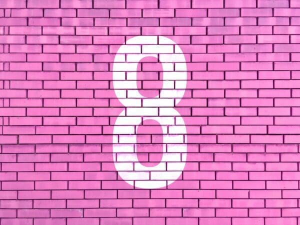 White number eight painted on a bright pink brick wall