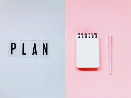 Plan spelled on grey background beside a notepad on a pink background