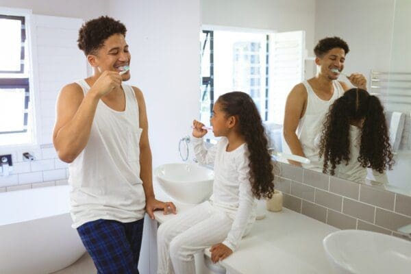 Father and daughter brushing teeth together in bathroom to form a habit