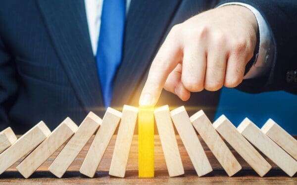 Businessman holding golden block to prevent others blocks from falling in a domino effect