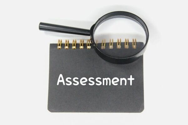 word assessment on a grey notebook with a magnifying glass on top